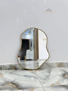 a mirror sitting on top of a marble floor next to a white wall with gold trim