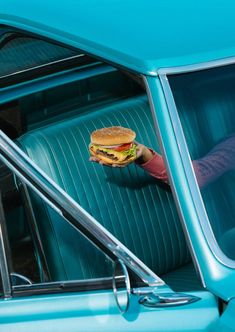 a person holding a hamburger in their hand while sitting in a car