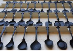 many spoons are lined up on the wall and one is black with silver handles