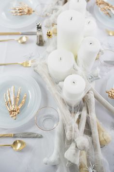 the table is set with white candles and gold utensils