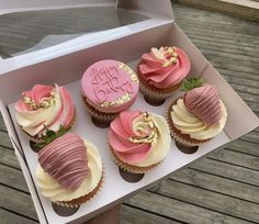 a box filled with pink and white cupcakes on top of a wooden table