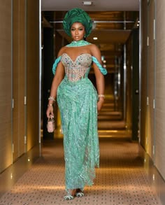 a woman in a green dress and headpiece walking down a hallway with a handbag