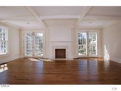 an empty living room with wood floors and white paint on the walls, windows, and fireplace