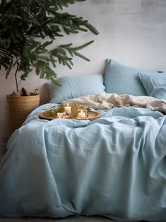 a bed covered in blue sheets with candles on the side and a potted tree behind it