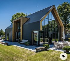 a modern house with large glass windows and wooden accents on the roof, along with an outdoor dining area