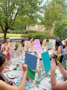 a group of people sitting around a table with paintings on it and paintbrushes in front of them