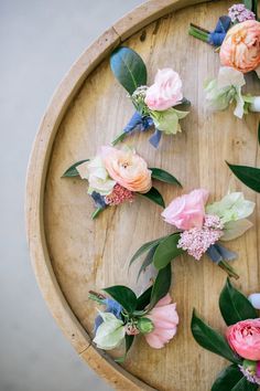 flowers arranged on a wooden tray with green leaves and pink roses in the center, surrounded by greenery