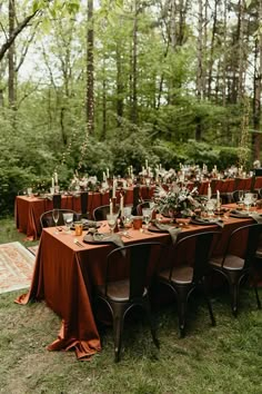 an outdoor dinner table set up with orange linens and place settings, surrounded by greenery