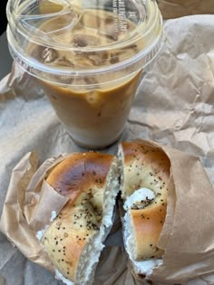 a bagel cut in half sitting on top of a piece of wax paper next to a cup of coffee