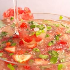 a glass bowl filled with watermelon and mint garnish next to strawberries