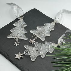 three silver christmas tree ornaments sitting on top of a slate slab