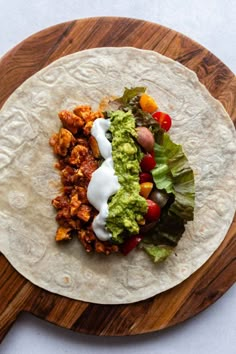 a tortilla topped with meat, lettuce and tomatoes on a wooden cutting board