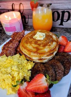 the breakfast plate is full of eggs, sausages, pancakes and strawberries next to a glass of orange juice