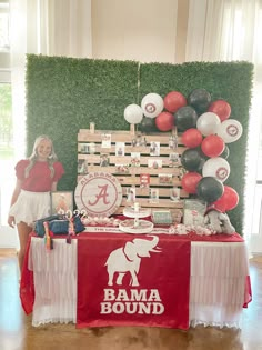 a woman standing next to a table with balloons and decorations on it, in front of a backdrop that says bama bound