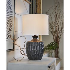 a table lamp sitting on top of a white dresser next to a painting and plant