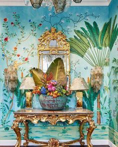 a blue room with gold furniture and flowers on the table in front of a mirror