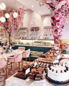 a table filled with cakes and desserts under pink flowers hanging from the ceiling in a restaurant