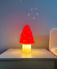 a red mushroom shaped lamp sitting on top of a white table next to a bed