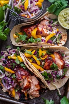 three fish tacos with slaw, peppers and cilantro on a baking sheet