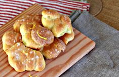 a wooden plate topped with donuts covered in icing and orange zest on top of a table