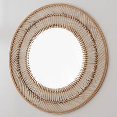 a circular mirror made out of bamboo sticks on a white wall with a reflection in it