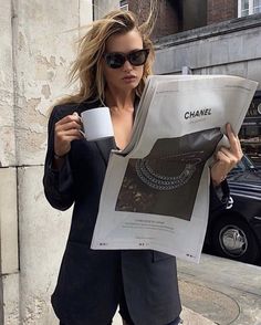 a woman holding a coffee cup and reading a newspaper