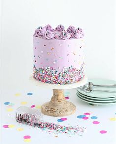 a pink cake with sprinkles is on a table next to plates and confetti