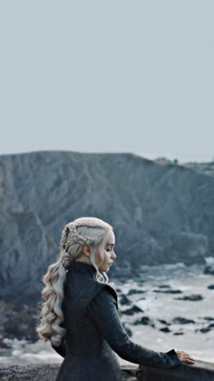 a woman with long hair and braids standing near the ocean