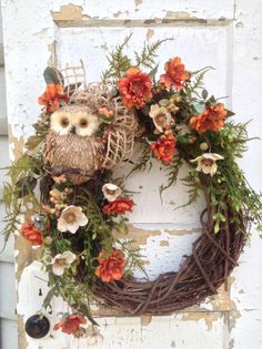 an owl sitting on top of a wreath with orange flowers and greenery around it