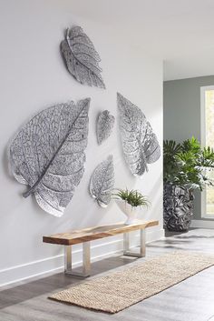 three metal leaves are hanging on the wall next to a bench and potted plant