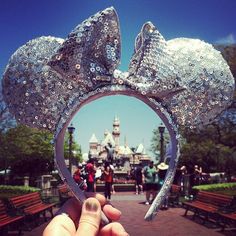 someone is holding up a mickey mouse head in front of the disney world castle at disneyland