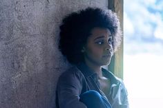 a woman leaning against a wall with her hand on her hip and looking off to the side