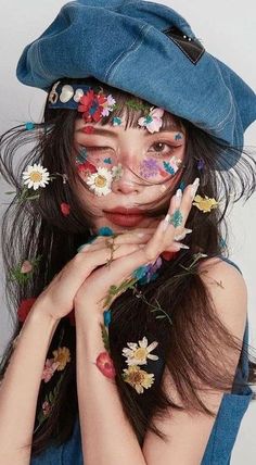 a woman with flowers painted on her face and hat over her head is posing for the camera