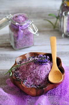 a wooden bowl filled with purple bath salts next to a jar of lavender essentials