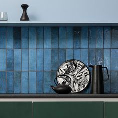 a kitchen with blue tiles and green cupboards on the counter top, black dishes in front of them