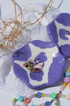 two purple and white dishes sitting on top of a lace covered table cloth next to a beaded necklace