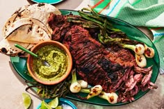 a plate with steak, asparagus and tortilla chips on it next to a bowl of guacamole