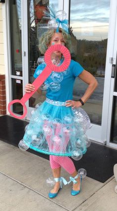 a woman in a costume holding a pink and blue object while standing on the sidewalk