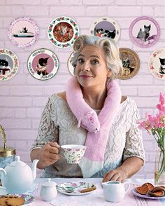 an older woman sitting at a table holding a cup and saucer