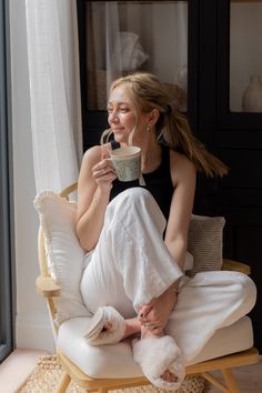 a woman sitting in a chair drinking from a cup