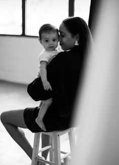 a woman sitting on top of a stool holding a baby