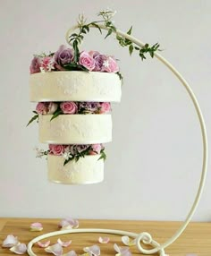 three tiered wedding cake with flowers on top, hanging from a white metal stand