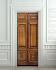 an empty room with two wooden doors and white walls, in the middle of it