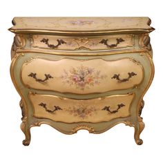 an ornately painted dresser with gold trimmings and flowers on the top, against a white background