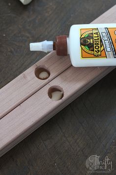 a bottle of glue sitting on top of a piece of wood next to two holes