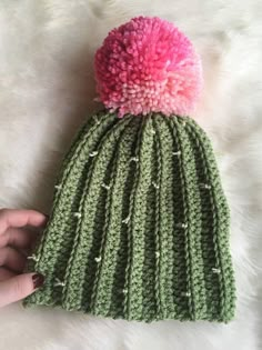 a hand holding a green and pink knitted beanie with pom - pom