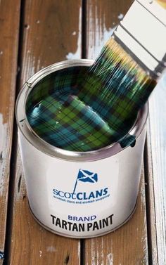 a can of tartan paint with a brush in it sitting on a wooden table