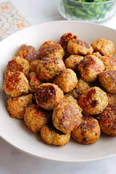 a white plate topped with meatballs next to a bowl of lettuce leaves