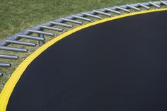 a black and yellow trampoline in the middle of a grassy area with metal bars