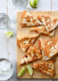 quesadilla slices on a cutting board with sour cream and limes